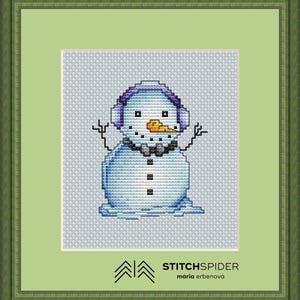 Könnte beinhalten: Kreuzstich-Kunst eines Schneemanns mit lila Ohrenschützern und einem grauen Schal, mit einer Karottennase und Stockarmen. Das Kunstwerk ist in einem grünen Holzrahmen gerahmt, mit dem Text "STITCHSPIDER" und dem Namen des Künstlers.