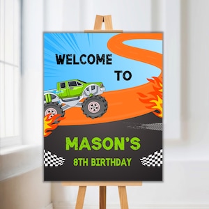 May include: A welcome sign for a monster truck themed birthday party. The sign features a green monster truck driving on an orange track with flames. The text on the sign reads "Welcome to Mason's 8th Birthday".