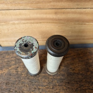 May include: Two vintage wooden spools with white thread wrapped around them. The spools have a dark brown wooden base and a light green and brown painted top.