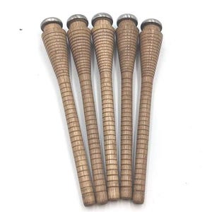 May include: Five wooden bobbins with a light brown finish and a ridged design. Each bobbin has a silver-colored metal cap on top. The bobbins are arranged vertically against a white background.