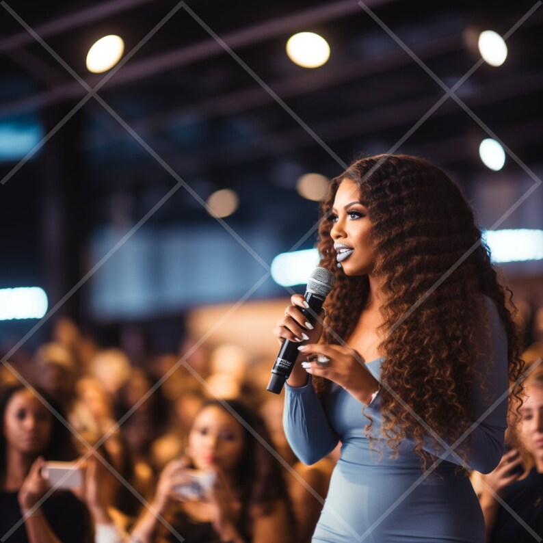 May include: A woman with long curly brown hair speaks into a microphone while wearing a light blue dress. She is speaking to a crowd of people.