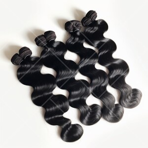 K&ouml;nnte beinhalten: Vier B&uuml;ndel schwarze Echthaarverl&auml;ngerungen in einer Body-Wave-Form. Das Haar ist f&auml;cherf&ouml;rmig angeordnet, wobei die Tressen sichtbar sind.