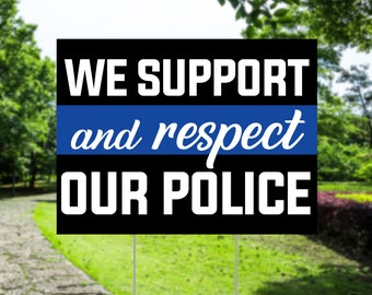 Pode incluir: Uma placa preta com texto branco que diz "APOIAMOS e respeitamos A NOSSA POLÍCIA" com uma faixa azul. A placa é exibida ao ar livre em um gramado.