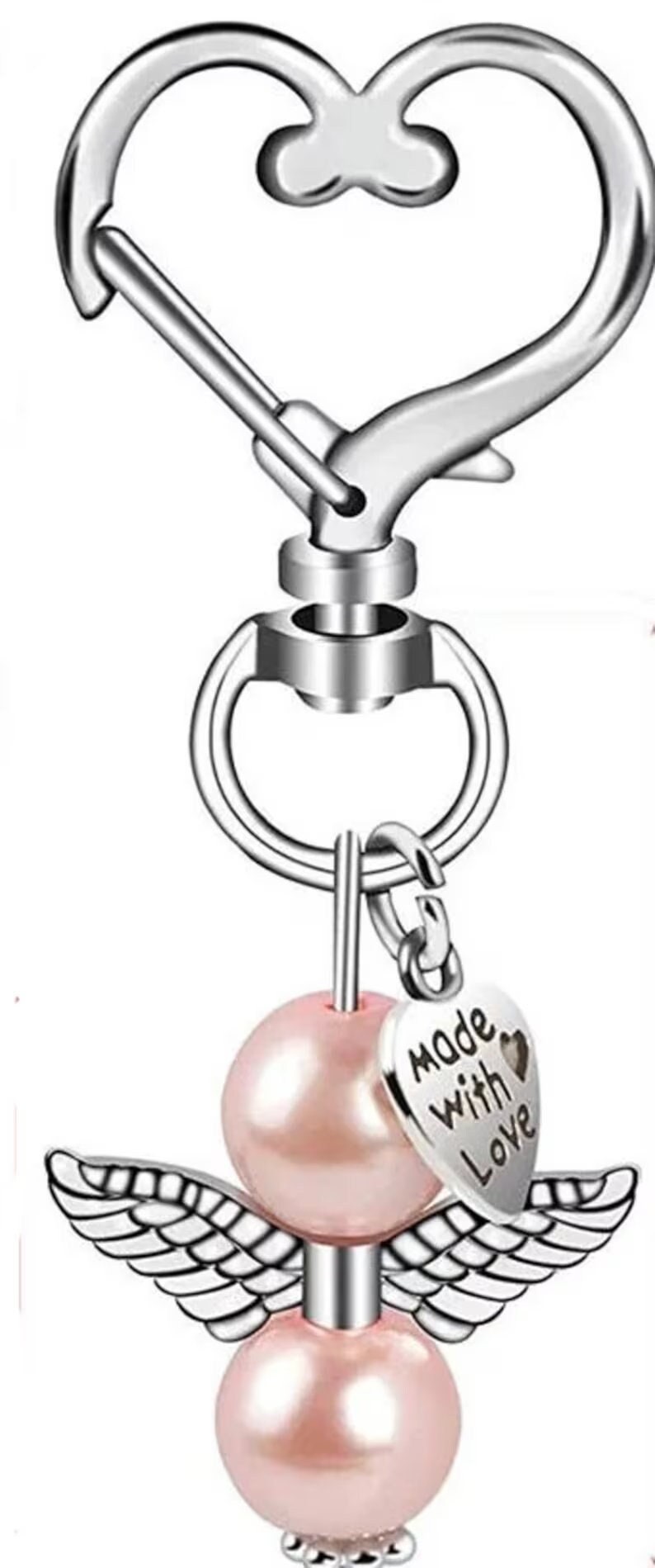 Op de afbeelding: Zilverkleurige sleutelhanger met een hartvormige sluiting. Voorzien van een roze parel engel bedel met zilveren vleugels en een hartvormige hanger met de tekst "Made With Love". Een charmant accessoire.
