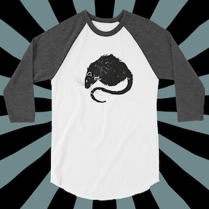 以下が含まれることがあります： 白とグレーのベースボールTシャツで、前面に黒いシルエットのネズミが描かれています。