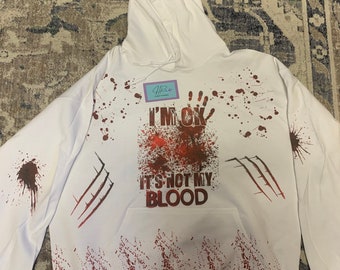 Pode incluir: Camisola de capuz branca com respingos de sangue vermelho e o texto "I'm OK It's not my blood".