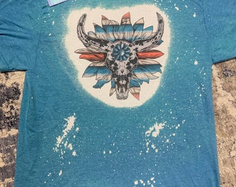 May include: A blue t-shirt with a white bleach design of a bull skull with a flower pattern. The shirt has a distressed look with white splatter paint.