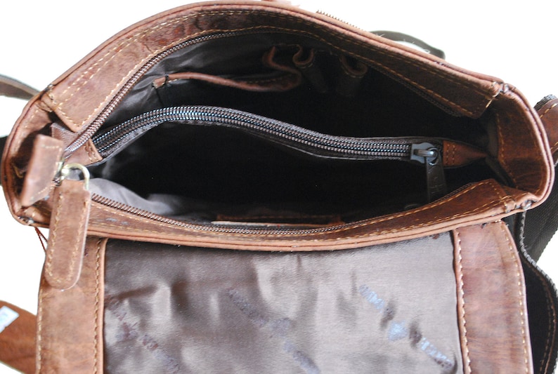 May include: The inside of a brown leather crossbody bag with a zippered pocket and a brown fabric lining.