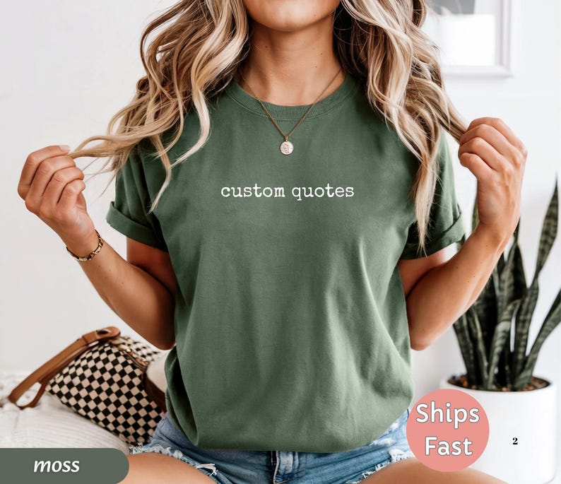 K&ouml;nnte beinhalten: Ein moosgr&uuml;nes T-Shirt mit dem wei&szlig;en Text "custom quotes". Das Shirt hat hochgekrempelte &Auml;rmel und wird mit blauen Jeansshorts getragen. Eine braune und schwarze karierte Tasche ist sichtbar.
