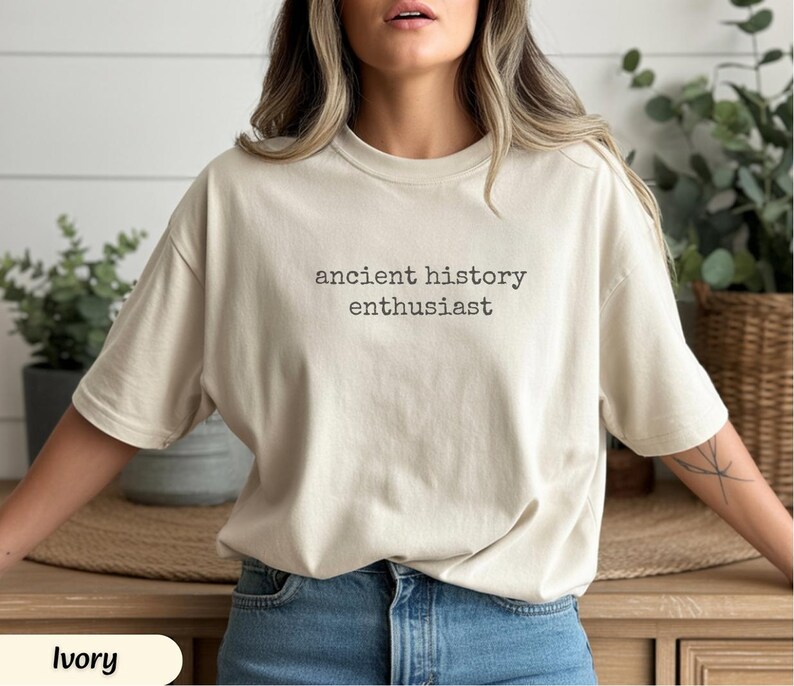 Pu&ograve; includere: T-shirt color avorio con la scritta "ancient history enthusiast" in nero. La maglietta ha una vestibilit&agrave; ampia ed &egrave; realizzata in un materiale morbido. La maglietta &egrave; abbinata a jeans blu.