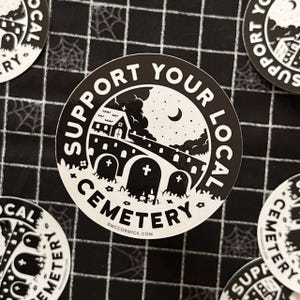 May include: Black and white sticker with a spooky illustration of a graveyard at night. The sticker says "Support Your Local Cemetery" with a small church, a bridge, and tombstones.