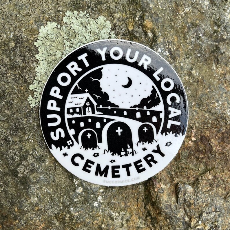 May include: Black and white sticker with the text "Support Your Local Cemetery" in a circle around a black and white illustration of a church, a graveyard, and a crescent moon.