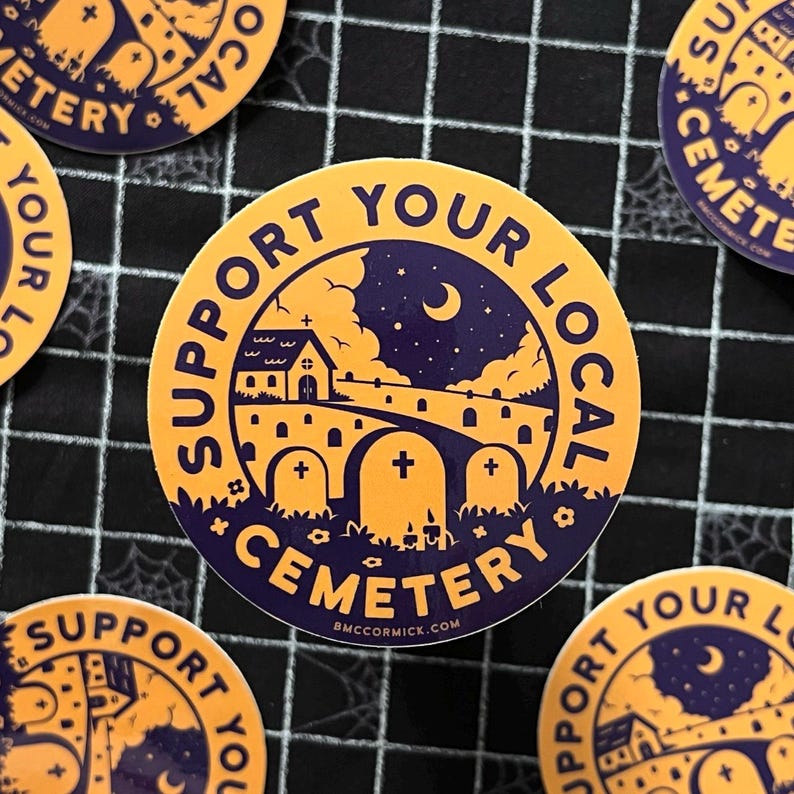 May include: A round sticker with a yellow background and purple text. The text reads "Support Your Local Cemetery". The sticker features a cartoon illustration of a church, a graveyard, and a crescent moon in the night sky.