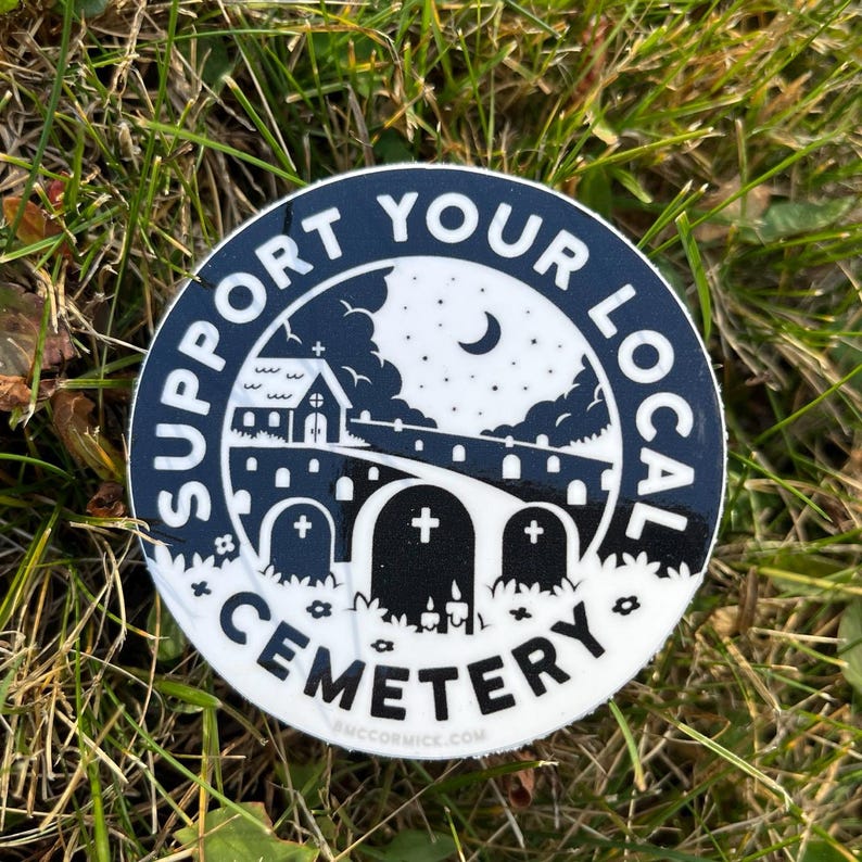 May include: A black and white sticker with the text "Support Your Local Cemetery" in a circle. The sticker features a small church, a crescent moon, and three tombstones.