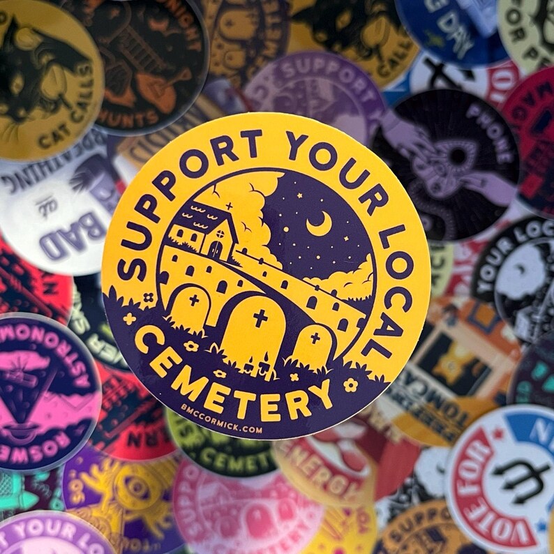 May include: A yellow and purple sticker with the text "Support Your Local Cemetery" and a graphic of a church, a moon, and a graveyard. The sticker is surrounded by other stickers with various designs.
