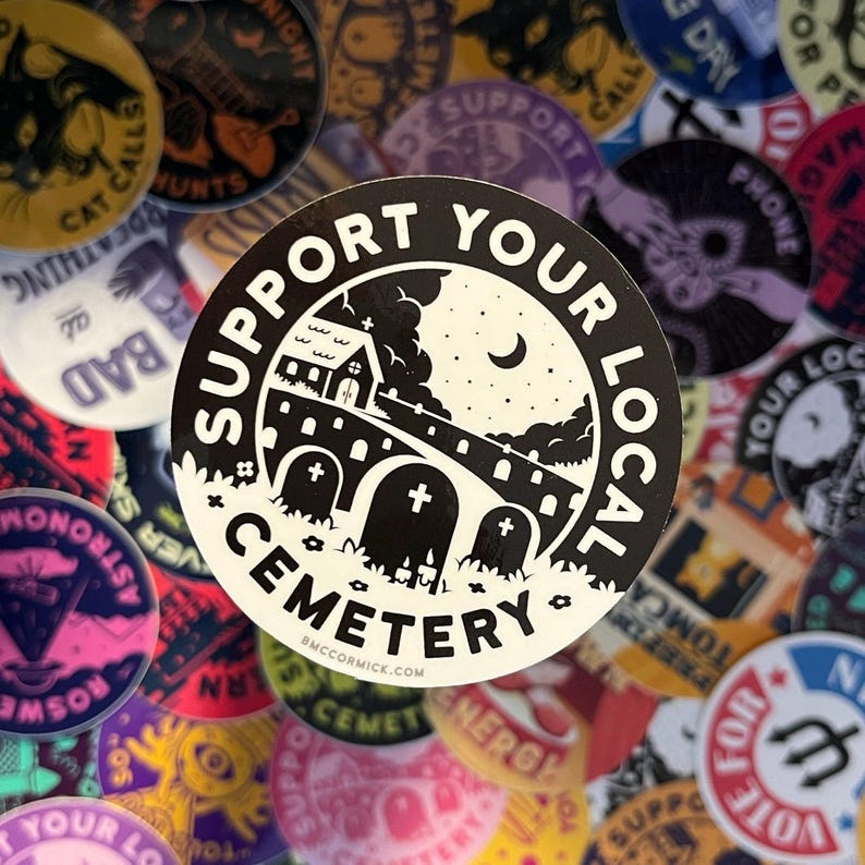 May include: A black and white sticker with the text "Support Your Local Cemetery" and a graphic of a small church, a bridge, and three tombstones. The sticker is surrounded by other colorful stickers.