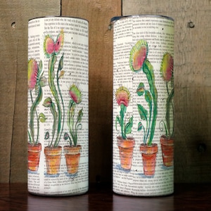 May include: Two stainless steel tumblers with a white background and a design of five carnivorous plants in pots. The plants are drawn in watercolour with green leaves and red, pink, and yellow flowers. The background is a page from a book.