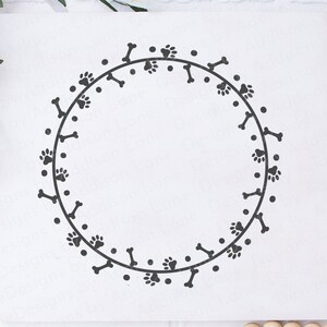 May include: A black and white dog bone and paw print wreath. The wreath is a circle with a white background. The wreath is perfect for a dog lover's home.