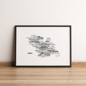 Op de afbeelding: Een zwart-wit afdruk in een zwarte lijst met een kaart van Sheffield, Engeland, samengesteld uit band- en artiestennamen. De print staat op een houten vloer tegen een witte muur.