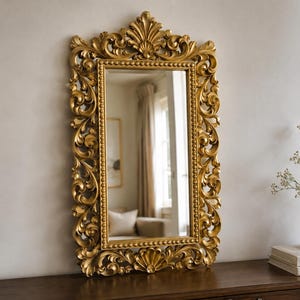 May include: A rectangular wall mirror featuring an ornate gold frame with intricate scrollwork and acanthus leaf carvings. The inner border of the frame is detailed with a beaded pattern, and the top and bottom edges are finished with shell motifs.