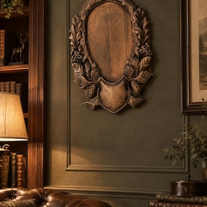May include: An oval wooden wall plaque featuring a central smooth panel surrounded by a carved border of oak leaves and acorns. The plaque has a shield-shaped base at the bottom and a dark brown finish with highlights that emphasize the texture.