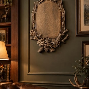Puede incluir: Una placa de pared con un panel ovalado central enmarcado por un borde decorativo de hojas de roble y bellotas esculpidas. La pieza presenta un acabado texturizado en tonos bronce con reflejos oscuros y detalles botánicos.
