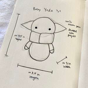 May include: Hand-drawn sketch of a Baby Yoda plush toy with measurements for height, width, and length. The caption reads "Baby Yoda plus" and "100% cotton yarn stuffed with polyfill".