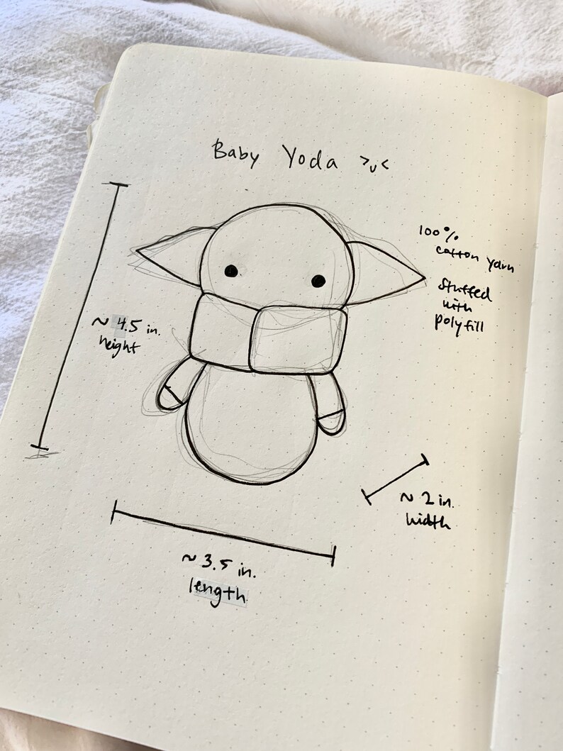 May include: Hand-drawn sketch of a Baby Yoda plush toy with measurements for height, width, and length. The caption reads "Baby Yoda plus" and "100% cotton yarn stuffed with polyfill".