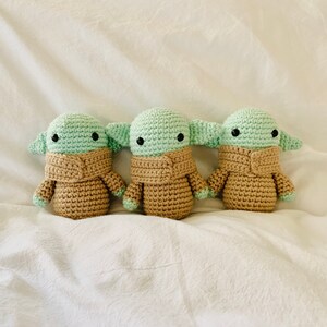 May include: Three crocheted plush toys in the shape of a popular fictional character. The toys are green and brown and have large eyes.