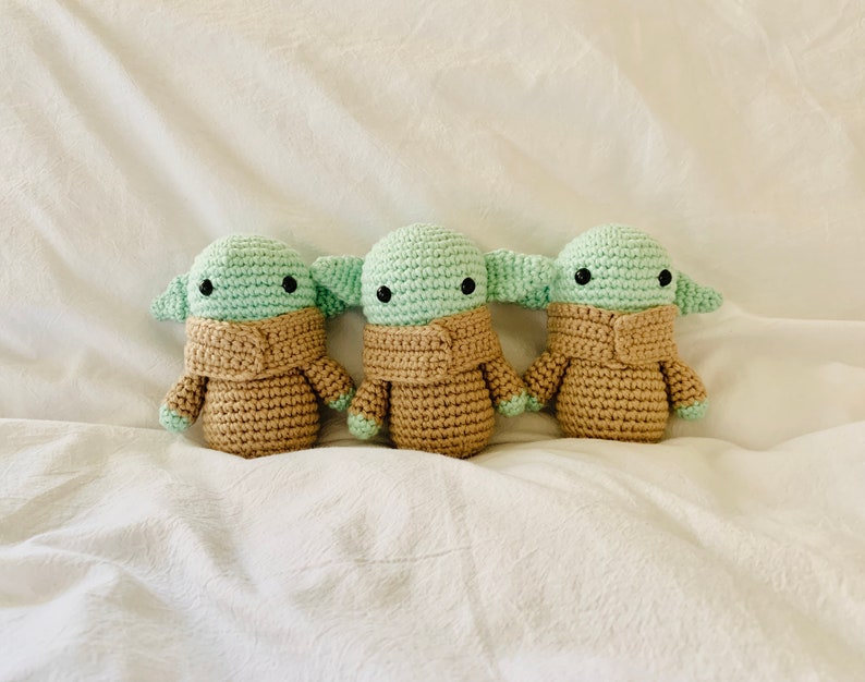 May include: Three crocheted plush toys in the shape of a popular fictional character. The toys are green and brown and have large eyes.