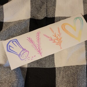 May include: A white sticker with a salt shaker, two sprigs of greenery, and a heart. The salt shaker is blue and purple, the greenery is green and yellow, and the heart is orange and pink.