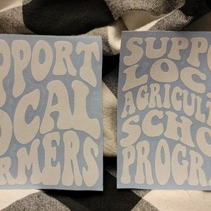May include: Two white vinyl stickers with a retro font design. The first sticker says "Support Local Farmers". The second sticker says "Support Local Agricultural School Programs".