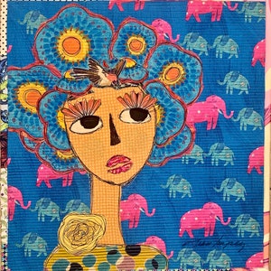 May include: A colorful mixed media artwork featuring a woman with a blue flower crown, large eyes, and a yellow flower on her neck. The background is a blue fabric with a pattern of pink and blue elephants.