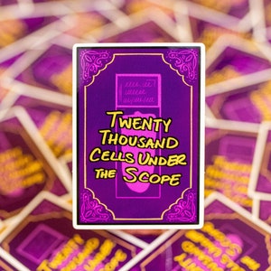 May include: A rectangular sticker with a purple background and gold border. The sticker features the text "Twenty Thousand Cells Under The Scope" in yellow and white. The sticker is surrounded by other stickers with the same design.