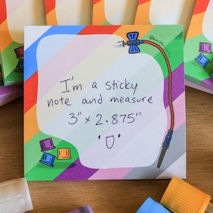 Peut inclure: Plusieurs blocs-notes adhésifs colorés avec un motif arc-en-ciel, mesurant 7,6 cm x 7,3 cm, et une note centrale avec du texte. L'image comprend également plusieurs tubes à essai avec des bouchons colorés, dispersés sur une surface en bois.