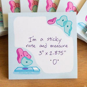 May include: Light blue sticky notes with a pink and teal illustration. The text on the front note reads, "I'm a sticky note and measure 7.6cm x 7.3cm". The notes are arranged on a wooden surface. A microscope is visible.