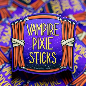May include: A sticker with the text "VAMPIRE PIXIE STICKS" in yellow, set against a purple starry background. The design includes bundles of orange sticks tied with white bands, framed by a purple border.