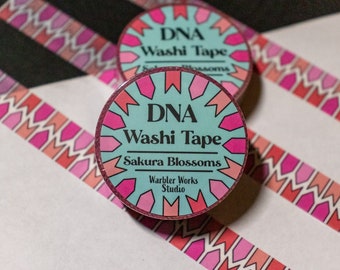 Könnte beinhalten: Zwei Rollen DNA Washi Tape mit dem Text "Sakura Blossoms", mit einem rosa-roten geometrischen Design. Die Bandrollen haben einen türkisfarbenen Hintergrund mit rosa Akzenten. Das Band liegt auf einer weißen Oberfläche.
