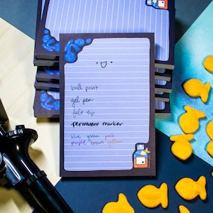 Peut inclure: Bloc-notes lignés avec un motif à rayures bleues et blanches. Le bloc-notes a une bordure marron foncé avec une illustration de bouteille. Le bloc-notes contient une liste d'instruments d'écriture. Des crackers en forme de poisson sont éparpillés.