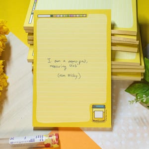 Peut inclure: Bloc-notes jaune avec des pages lignées, mesurant 10x15 cm. Le bloc-notes a une bordure décorative et une petite illustration d'un pot. Le texte sur le bloc-notes se lit : "I am a memo pad, measuring 4x6" (non sticky)."