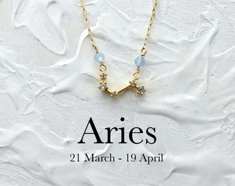 May include: Gold necklace with a constellation design featuring small clear stones and light blue beads. The necklace is on a white background with the text "Aries 21 March - 19 April".