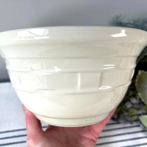 May include: A cream-colored ceramic mixing bowl with a wide, flared rim and a textured basket-weave pattern embossed around the exterior. The bowl features a smooth, glossy finish and a rounded base, designed for kitchen use and food preparation.