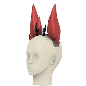 Puede incluir: Un tocado rojo y negro con un diseño diabólico. El tocado presenta tres cuernos rojos grandes y puntiagudos y varios cuernos negros más pequeños. El tocado se usa en una cabeza de maniquí.