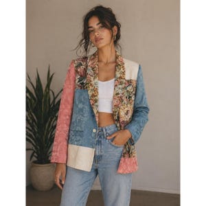 May include: A patchwork blazer featuring a mix of solid pink, blue, and cream panels alongside floral patterned lapels. The garment has a single front button closure, long sleeves, and a structured fit, worn over a plain white tank top and blue jeans.