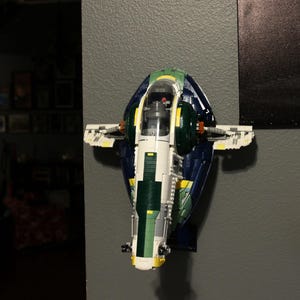 Puede incluir: Una nave espacial Lego azul, verde y amarilla con una cabina transparente. La nave espacial está montada en una pared.
