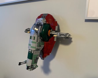 May include: A green and red Lego model of a spaceship, the Slave I, from the Star Wars franchise. The model is mounted on a wall.