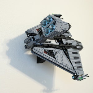 Puede incluir: Maqueta de nave espacial gris y negra construida con ladrillos de juguete. El modelo presenta cuatro motores iluminados en azul y est&aacute; montado en una pared blanca. La nave espacial tiene un dise&ntilde;o detallado con varios &aacute;ngulos y formas.