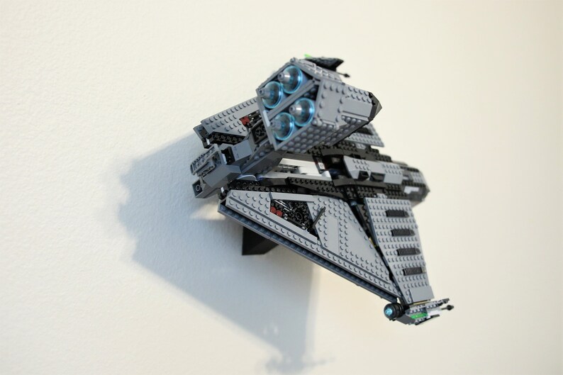 Puede incluir: Maqueta de nave espacial gris y negra construida con ladrillos de juguete. El modelo presenta cuatro motores iluminados en azul y est&aacute; montado en una pared blanca. La nave espacial tiene un dise&ntilde;o detallado con varios &aacute;ngulos y formas.