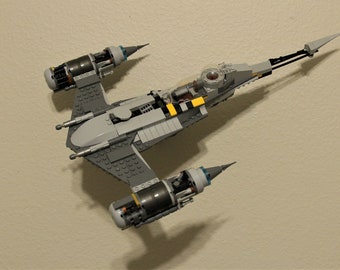 May include: A gray and black Lego spaceship with yellow accents. The spaceship has two engines on the bottom and a long, thin tail.