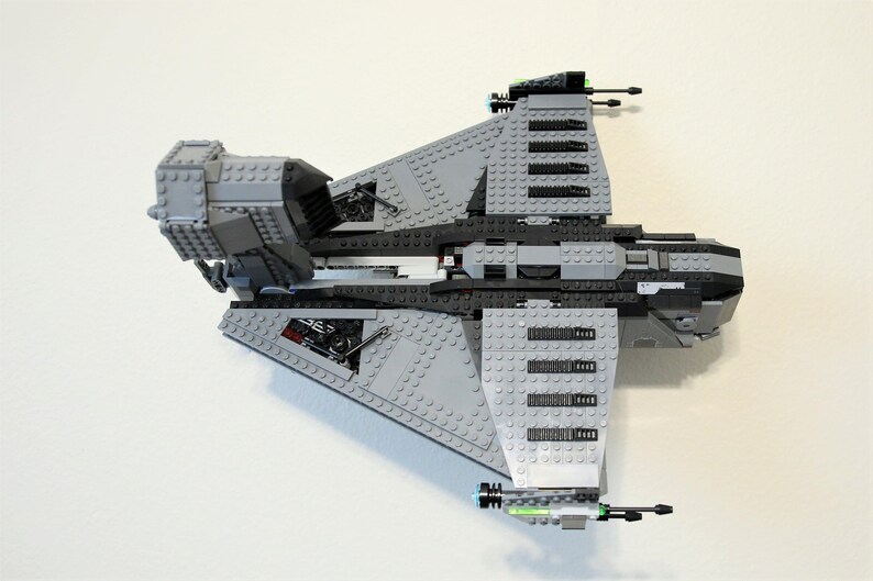 Puede incluir: Maqueta de nave espacial gris y negra construida con ladrillos de juguete entrelazados. El modelo presenta alas anguladas, m&uacute;ltiples torretas de ca&ntilde;&oacute;n y elementos estructurales detallados. El juguete est&aacute; sobre un fondo blanco.